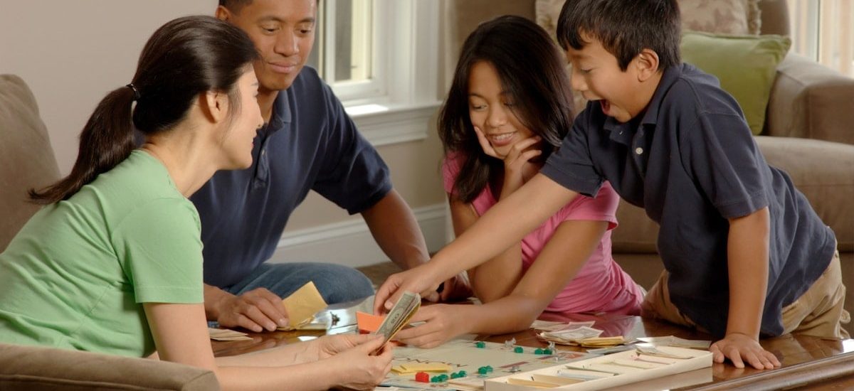 Family Playing A Board Game. An Asian family (adult male and female and two adolescents, male and female) sitting around a coffee table playing a board game. Photographer Bill Branson