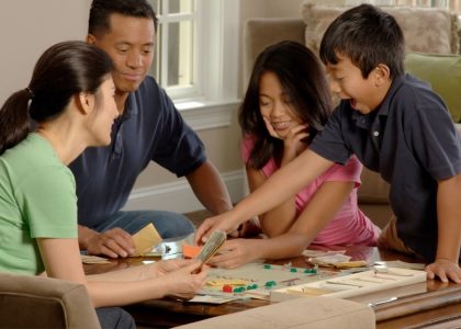 Family Playing A Board Game. An Asian family (adult male and female and two adolescents, male and female) sitting around a coffee table playing a board game. Photographer Bill Branson